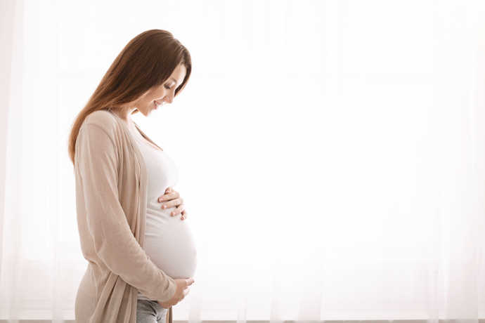 Embarazada de perfil, feliz sujetando y mirándose la barriga