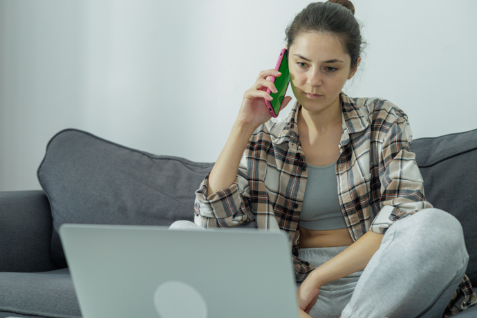 mujer joven e el sofá con el celular y el ordenador a la vez