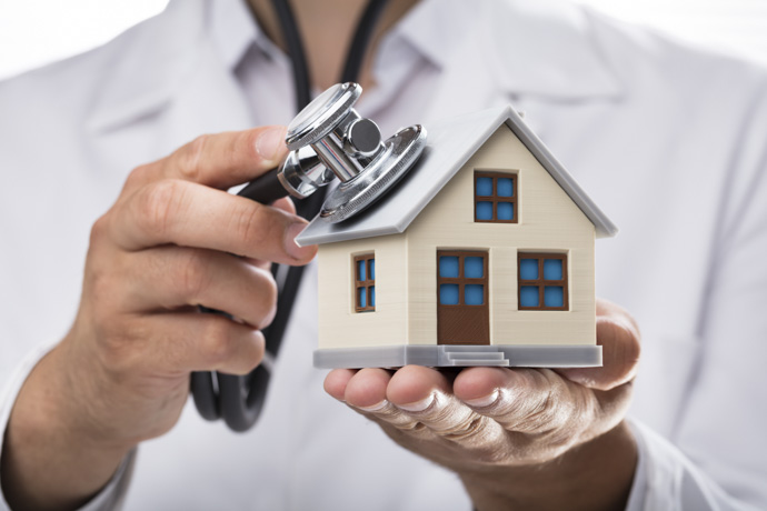 Profesional de la salud sosteniendo una casa en miniatura y un estetoscopio representando el servicio de hospitalización domiciliaria
