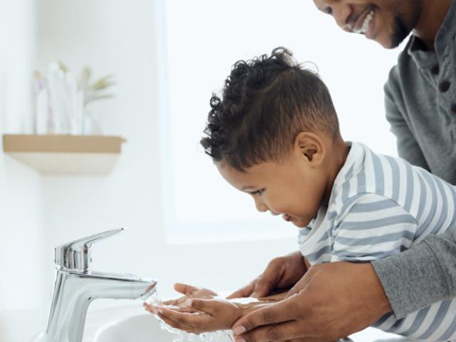Padre lavando las manos a su hijo pequeño, uno de los hábitos de higiene más importantes para la salud. 